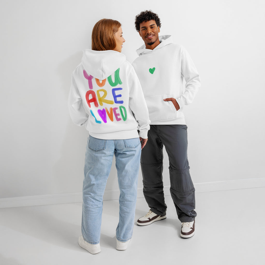Two people wearing white hoodies with colorful text and a green heart design.